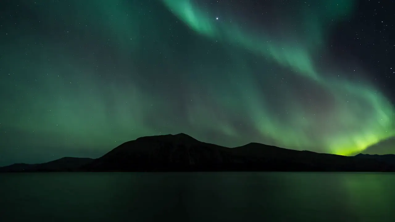 Emerald northern lights above a dark mountain landscape